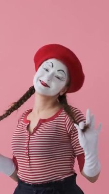 Pembe arka planda bir portrede pozitif ve arkadaş canlısı bir kadın, sıcak ve anlamlı jestlerle iyi bir ruh hali yayıyor. Dikey video.