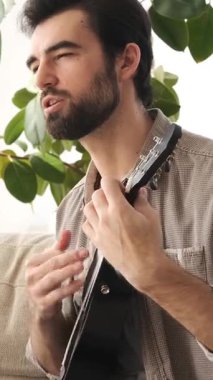 Dostum, bir müzisyen, evde boş zamanlarında gitar çalıyor, müzikten tatmin oluyor, rahat bir ortamda rahatlatıcı ve yaratıcı bir hobiye dalmış. Dikey video.