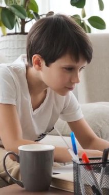 Evde e-öğrenim ve ödev olarak dizüstü bilgisayar kullanan özenli bir öğrenci, sessiz bir çalışma alanında eğitime odaklanıyor. Dikey video.