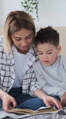 Anne evde çocuklarla kitap okuyarak rahatlıyor, rahat bir ortamda çocukluk deneyiminin tadını çıkarıyor. Dikey video.