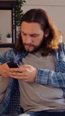 Akşamları evde akıllı telefondan mesajlaşan, internet iletişimine dalmış, rahat bir ortamda bağlantılarını sürdüren konsantre bir adam. Dikey video.