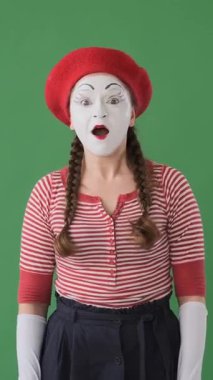 Neşeli pandomimci dansçı yeşil arka planda başparmağını kaldırıyor, canlı ve ilgi çekici performansla anlaşmayı ifade ediyor. Dikey video.