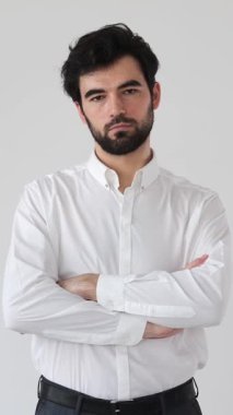 Beyaz arka planda bir portrede ciddi ve kendinden emin bir adam, düşünceli bir ifadeyle kameraya bakıyor, kişiliği vurguluyor ve davranışlarına odaklanıyor. Dikey video.
