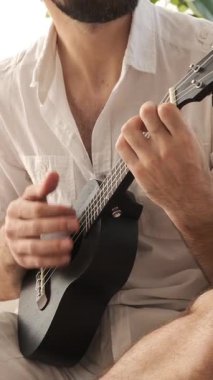 Bir adamın, bir müzisyenin yakın çekimi, evde bir gitarla müzik çalmak, eğlenmek, rahat bir ortamda tatmin edici bir müzik arayışına dalmak. Dikey video.