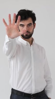Ciddi bir adam, beyaz arka planda bir avuç içi ile, hayal kırıklığını, korumayı ve katı ve net bir tavırla anlaşmazlığı ifade eden bir dur hareketi sergiliyor. Dikey video.