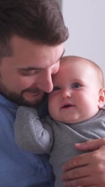 Portrait of a positive father playing with toddler baby in home bedroom. Babyhood, childhood and adolescence concept. Vertical video.