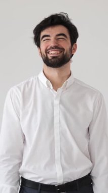 Beyaz arka planda bir portrede neşeli ve oyuncu bir iş adamı. Canlı ve çekici bir ifadeyle bireysellik, zevk ve keyif yayıyor. Dikey video.