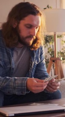 Ciddi bir adam evde nakit para sayıyor, zenginlik ve bütçe yönetimine odaklanıyor, özel bir ortamda disiplinli bir yaklaşımla karla başa çıkıyor. Dikey video.