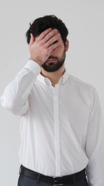 Üzgün adam beyaz arka planda bir facepalm hareketi yapar, başarısızlığı, utancı ve mağlubiyeti açık ve anlaşılır bir hüsranla ifade eder. Dikey video.