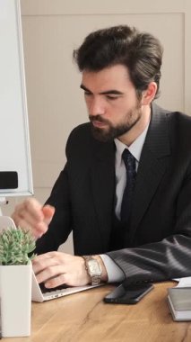 Ofiste dizüstü bilgisayarla çalışan kafası karışmış bir çalışan, mesajlaşırken ve sohbet ederken dahiyane bir fikir üretiyor, profesyonel bir ortamda yaratıcı bir şekilde katkıda bulunuyor. Dikey video.