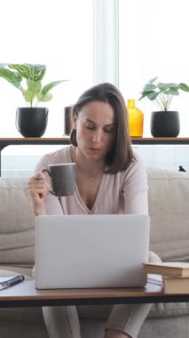 Ciddi bir kadın evde dizüstü bilgisayarla çalışıyor, uzaktan işgali yönetiyor ve kendini yapılandırılmış bir çalışma alanına adamış. Dikey video.