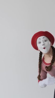 Neşeli pandomim sanatçıları birlikte beyaz arka planda el sallayarak neşeli ve anlamlı jestlerle dostça bir selam veriyorlar. Dikey video.