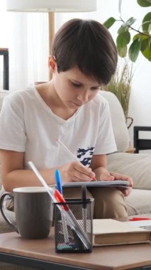 Düşünceli çocuk bir deftere yazıyor, evde ödev yapıyor ve öğreniyor, eğitime odaklanıyor ve kendini işine adıyor. Dikey video.