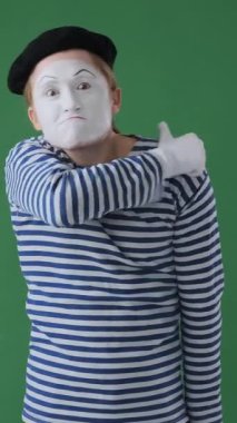 Öfkeli pandomimci, yeşil arka planda yumruklarıyla tehditler savurarak şiddetli ve güçlü hareketlerle saldırıyor. Dikey video.