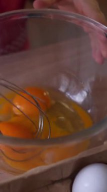 Evdeki mutfakta yemek hazırlarken kasede yumurta karıştıran bir çocuğun yakın çekimi, özenle mutfak hazırlıklarına odaklanıyor. Dikey video.