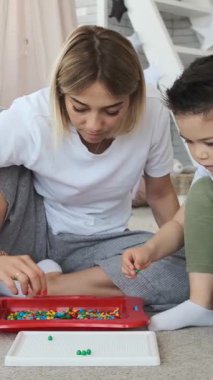 Anne ve oğlu evde bir mozaikle oynuyorlar, eğleniyorlar, sıcak ve iç mekanlarda yaratıcı bir şekilde iş birliği yapıyorlar. Dikey video.
