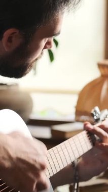Evde gitar çalan, zevk ve rahatlıkla meşgul olan, rahat ve huzurlu bir ortamda müzikten hoşlanan tatmin olmuş bir adam. Dikey video.