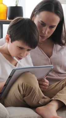 Evde bir defterde ödevlerini yapmaya odaklanmış anne ve okul çocuğu, kendini adamış bir öğrenme alanında çalışma ve egzersiz yapıyor. Dikey video.