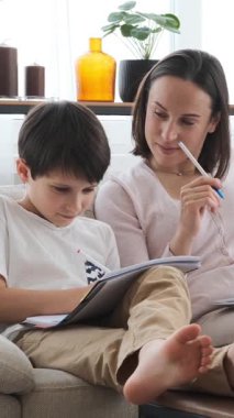 Mutlu anne ve oğul birlikte öğreniyor, ev ödevlerini ve egzersizlerini tamamlıyor, destekleyici bir ortamda zevkle eğitime girişiyor. Dikey video.