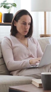 İnternette dizüstü bilgisayar ve belgelerle çalışan ciddi bir kadın. Yapılandırılmış çalışma alanına odaklanarak finansal strateji yönetiyor. Dikey video.
