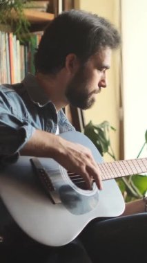 Evde gitar çalan bir adam, eğlenmek için eğlence ve tatmin bulmak, müzikle rahat ve keyifli bir atmosfer yaratmak. Dikey video.