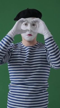 Çizgi roman sanatçısı yeşil arka planda el dürbünü kullanıyor, oyuncu ve çekici bir hareketle merak ve buluş sergiliyor. Dikey video.