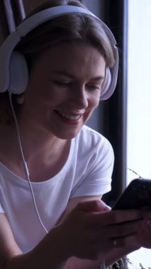 Evdeki dijital boş zamanlarında sosyal medyada mesajlaşmak için telefon kullanan neşeli bir kadın, neşeli online nişanı kucaklıyor. Dikey video.