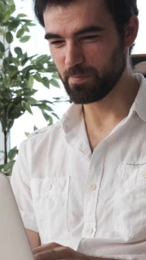 İnternette çalışan ya da evde bilgisayarla uzaktan öğrenim gören, neşeli bir zihniyetle iletişim ve eğitime odaklanan olumlu bir adam. Dikey video.