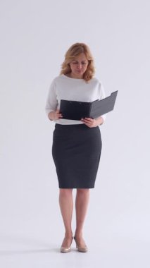 Beyaz bir arkaplanda belgelerle çalışan odaklanmış bir kadın, yoğun ve profesyonel bir tavırla finans, iş ve muhasebe genel bir bakış açısına sahip. Dikey video.