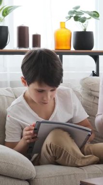 Evde bir defterle ödev yapmaya odaklanmış bir çocuk, e-öğrenme ve sessiz bir eğitim ortamında kendini adama dersleri alıyor. Dikey video.