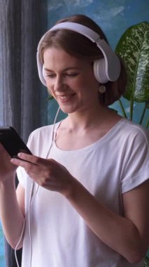 Evde boş zamanlarında müzik dinleyen ve dans eden mutlu bir kadın, rahat bir ortamda canlı enerjiyle şık bir rahatlığın tadını çıkarıyor. Dikey video.