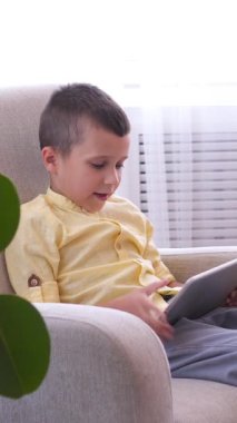 Evde internet eğlencesi için tablet kullanan olumlu oğul ve anne, rahat bir dijital ortamda coşkuyla çevrimiçi keyif alıyorlar. Dikey video.