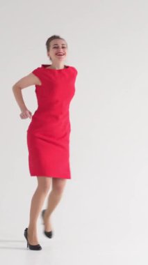 Pozitif kadın dans ediyor ve beyaz arka planda eğlenmeyi seviyor, enerjik ve neşeli hareketlerle bir disko partisinin ürpertici havasını kucaklıyor. Dikey video.