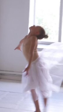 Elbiseli bir kız stüdyoda eğitim sırasında dans provası yapar, jimnastik öğelerine ve zarafet ve dansa adanmışlıkla ders tabanlı koreografiye odaklanır. Dikey video.