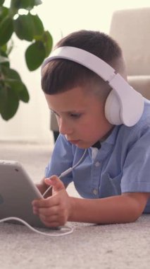 Konsantre çocuk evde bir tablet bilgisayarla çevrimiçi boş vakit geçiriyor, rahat bir dijital ortamda eğlence ve iletişim üzerine odaklanıyor. Dikey video.