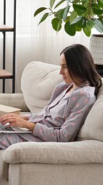 Dost canlısı bir kadın evde dizüstü bilgisayar kullanarak sohbet ediyor, sıcak ve ulaşılabilir bir tavırla teknoloji aracılığıyla iletişim ve bağlantı kuruyor. Dikey video.