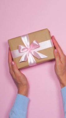 Kadın pembe arka planda bir hediye ya da hediye kutusu tutuyor ve özel bir an için hazırlanmış sıcak bir karşılama ya da hoş geldin sürprizi sunuyor. Dikey video.