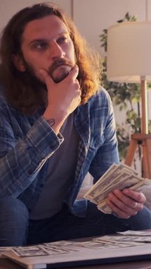 Nakit sayan ve evde bütçe planlayan bir adam, finans ve kaynakları düşünen, odaklanmış bir ortamda özenle mali meseleleri organize eden biri. Dikey video.