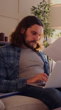 Evde dizüstü bilgisayar ve evrak işleriyle uğraşan, muhasebe ve teftiş işleriyle uğraşan özenli bir serbest çalışan. Dikey video.