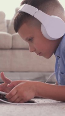 Evde boş zamanlarında internet ve çevrimiçi eğlence için tablet bilgisayar kullanan ve rahat bir ortamda canlı bir dijital deneyimin tadını çıkaran çocuk. Dikey video.