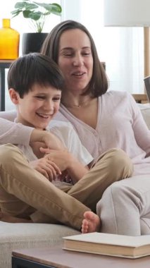 Arkadaş canlısı anne ve oğul birlikte boş zamanlarını evde televizyon izleyerek paylaşılan rahatlığın tadını çıkararak geçiriyorlar. Dikey video.