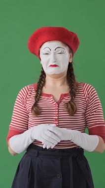 Mutsuz kadın pandomimci yeşil arka planda komik bir yetenekle ağlıyor, üzüntü ve duygusal gerginlik dolu jestlerle stresi ifade ediyor. Dikey video.