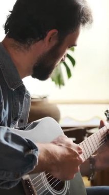 Evde gitar çalan, eğlence ve eğlenceye dalan, müzikten keyif alan ve rahatlatıcı bir performans sergileyen bir adam. Dikey video.