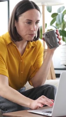 Ciddi bir kadın evde dizüstü bilgisayarla çalışıyor, iş ve muhasebe işleriyle uğraşıyor ve ev içinde düzenli bir çalışma alanına odaklanıyor. Dikey video.