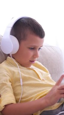 Evde internet keyfi için tablet kullanan memnun çocuk, bir kanepede dinleniyor, siber alanın tadını çıkarıyor ve rahat bir dijital ortamda dinleniyor. Dikey video.