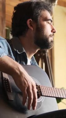 Gitar çalan ve evde şarkı söyleyen bir adam, eğlenceli bir eğlence ortamı yaratıyor, eğlenceli ve rahat bir atmosfer yaratıyor ev ortamında müzik eşliğinde. Dikey video.
