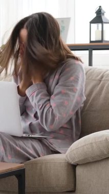 Sağlıksız bir kadın evde dizüstü bilgisayarla eğlenirken hapşırıyor, rahat ama zorlu bir ortamda hastalık ve hastalıkla uğraşıyor. Dikey video.