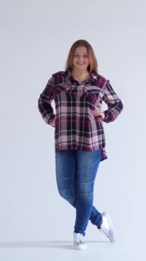 Beyaz bir arkaplan karşısında rahat ve cana yakın bir kadın, sakin ve cana yakın bir tavırla kişilik, memnuniyet ve zevk sergiliyor. Dikey video.