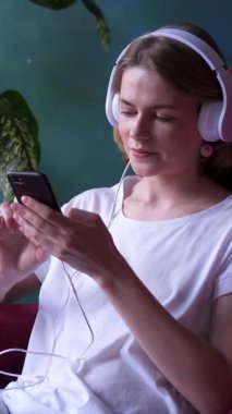 Mutlu bir kadın internet eğlencesi ve evde online eğlence için akıllı telefon kullanıyor. Dijital aktivitelere hevesle katılıyor. Dikey video.