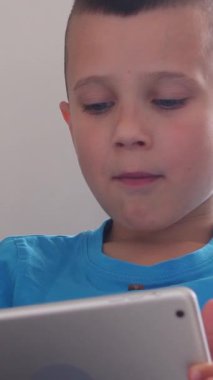 Evde bir tabletle çevrimiçi boş vakit geçirirken atıştırmalık bir şeyler yiyen neşeli ve rahat dijital eğlencenin tadını çıkaran bir çocuk. Dikey video.